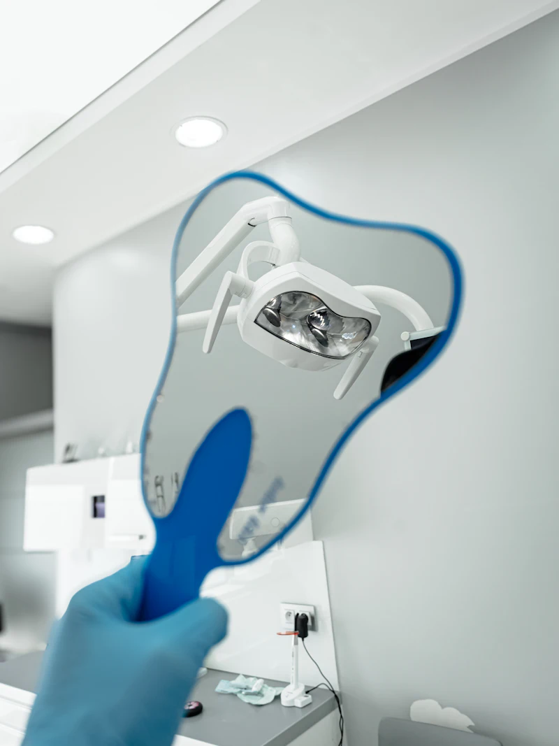 A gloved hand holding a tooth-shaped hand mirror in a dental room
