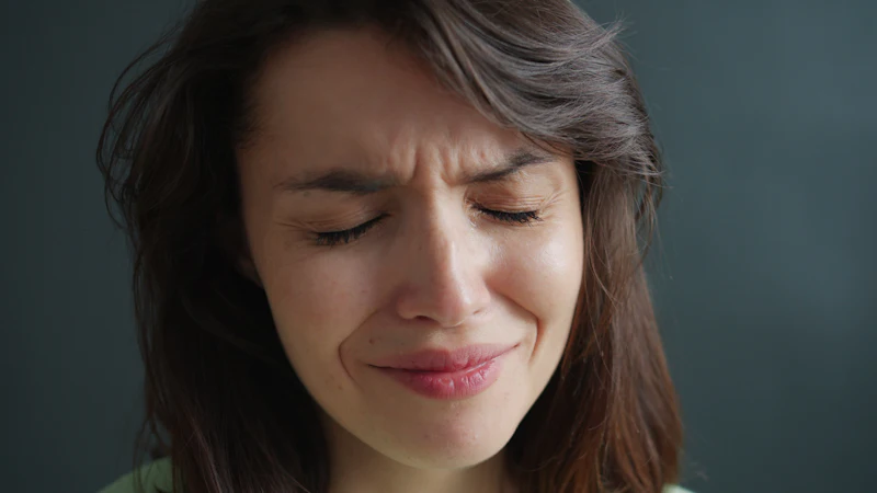 A young woman wincing in pain with her eyes shut